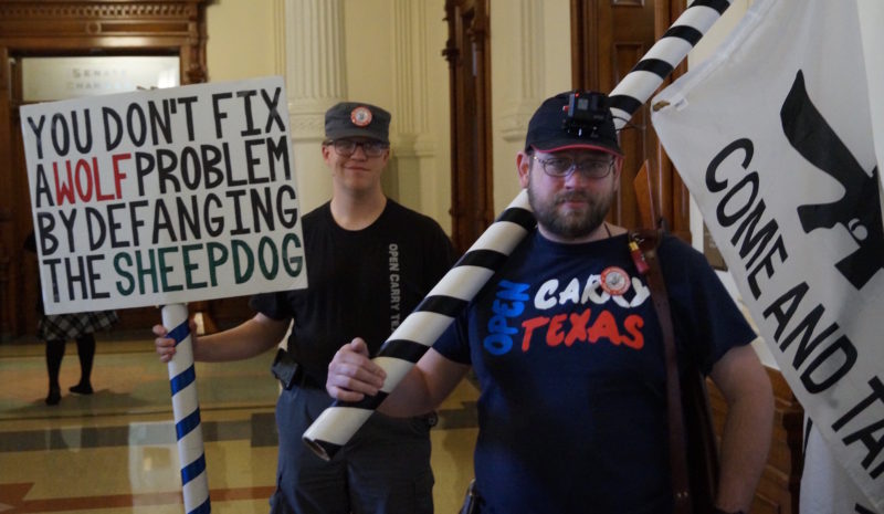 Gun rights activist in an Open Carry Texas t-shirt carrying a banner saying "Come and Take It" with a rifle on it, demonstrating inside the Texas Capitol