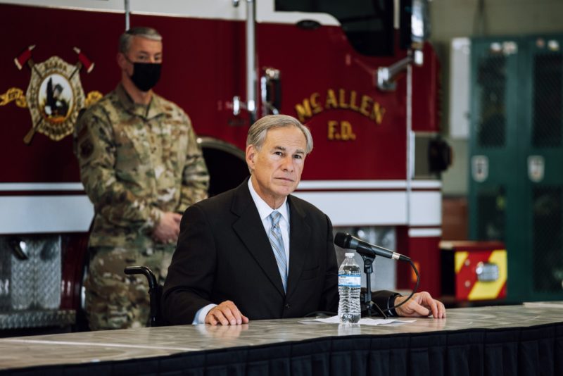 Greg Abbott at a vaccination outreach event with a National Guard soldier in a face mask and a fire truck behind him.